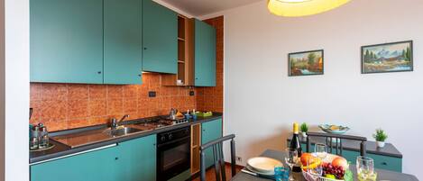 Une cuisine moderne avec des armoires de couleur turquoise, une cuisinière à gaz et un coin repas avec une table dressée pour quatre personnes.