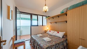 A bedroom with a bed, a chair, a wardrobe, a bedside table with a lamp, and a window with curtains. - Acqua Marina 800 M Dal Mare (Cogoleto)