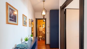 A hallway with framed artwork on the walls, a blue counter with a telephone and a plant, and a bathroom visible through an open door. - Acqua Marina 800 M Dal Mare (Cogoleto)