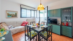 A dining area with a table set for four, a sofa, a kitchen with green cabinets, and a painting on the wall. - Acqua Marina 800 M Dal Mare (Cogoleto)