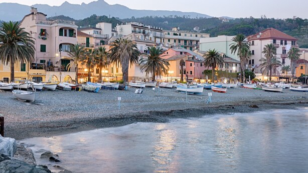A coastal town with boats docked along the shore, buildings with balconies, and palm trees. - Acqua Marina 800 M Dal Mare (Cogoleto)