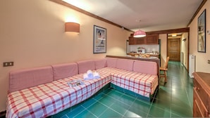 A cozy living room with a checkered sofa, a kitchen area, and a hallway. - Grange Hike Ski - 24C Sestriere (Sauze di Cesana)