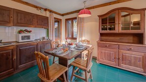 A kitchen with wooden cabinets, a dining table with chairs, a microwave, and a hanging light fixture.