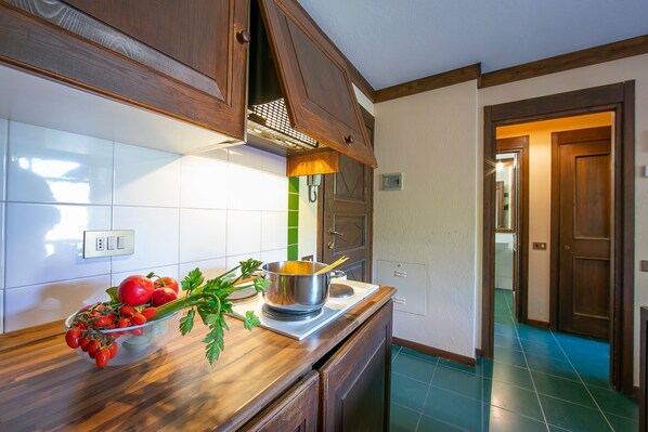 A kitchen with wooden cabinets, a stove, and a bowl of tomatoes and parsley on the counter. - Grange Hike Ski - 4C Sestriere (Sauze di Cesana)