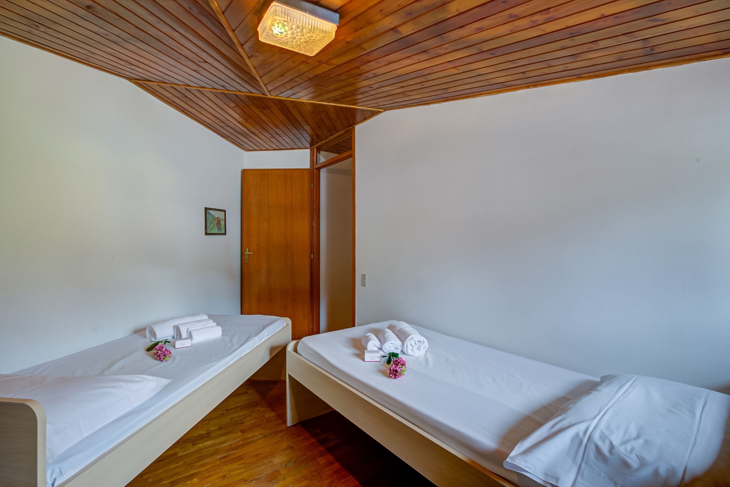 A room with two single beds, wooden ceiling beams, white walls, and a wooden door.