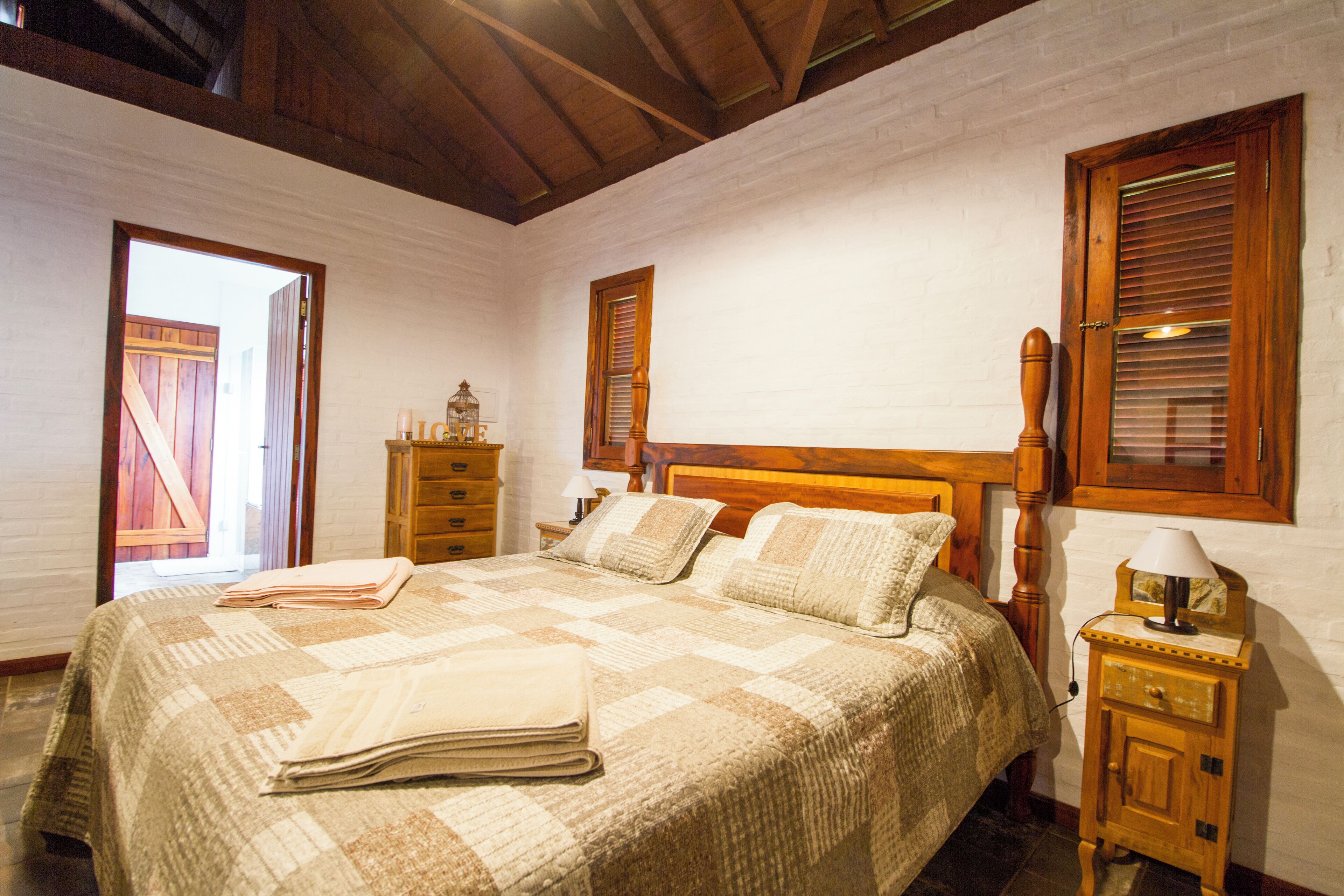 Un dormitorio con una cama de madera, una mesita de noche con lámpara y una ventana con contraventanas de madera.