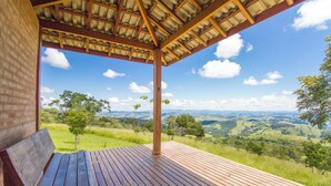 A wooden deck with a bench, a brick wall, and a view of a green landscape under a clear sky. - Magnificat Cottage (Cunha)