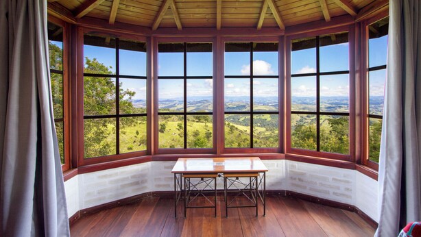 A corner room with a wooden ceiling and large windows offering a view of a green landscape. - Magnificat Cottage (Cunha)