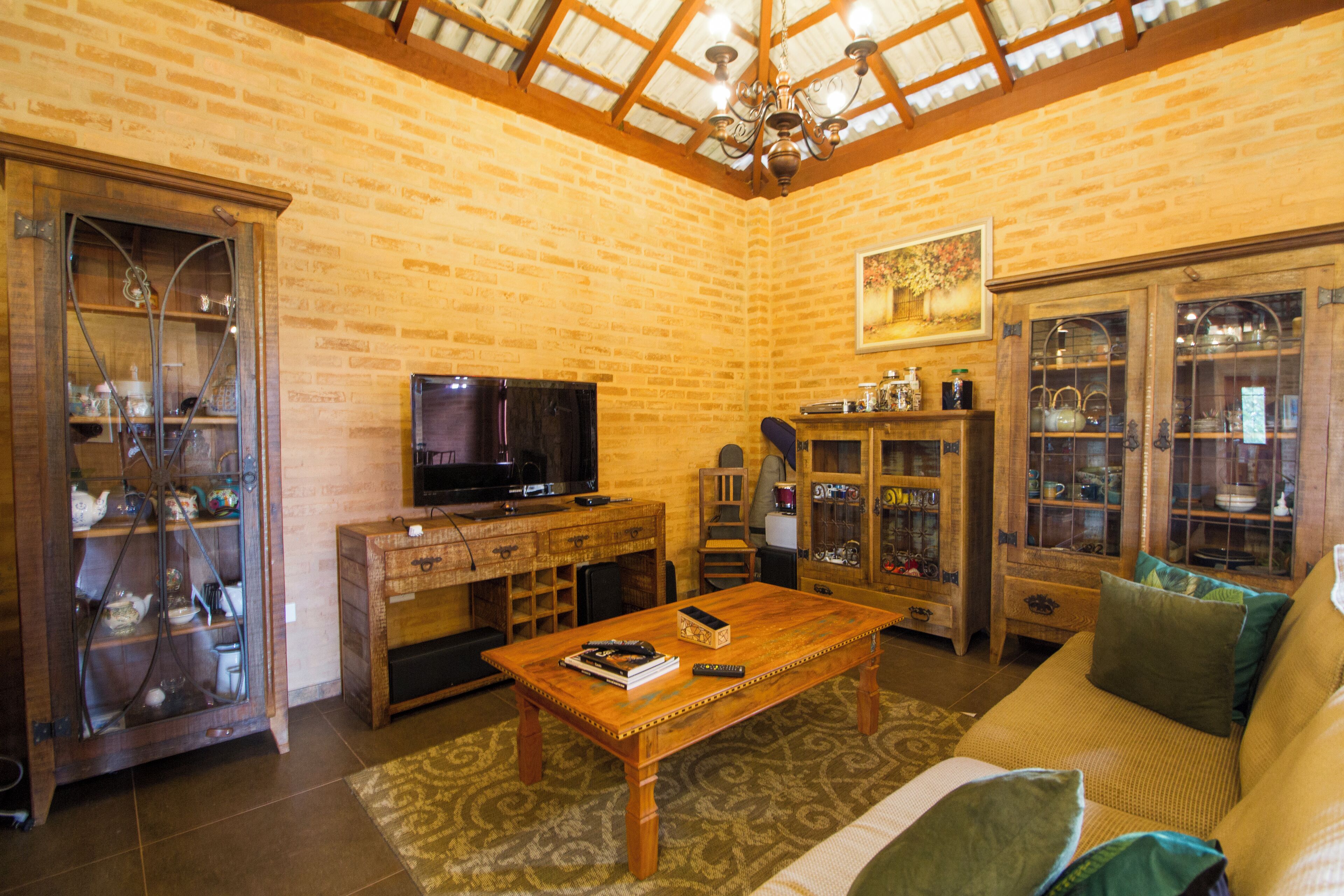 Uma sala de estar aconchegante com parede de tijolos, móveis de madeira, uma televisão e um lustre.