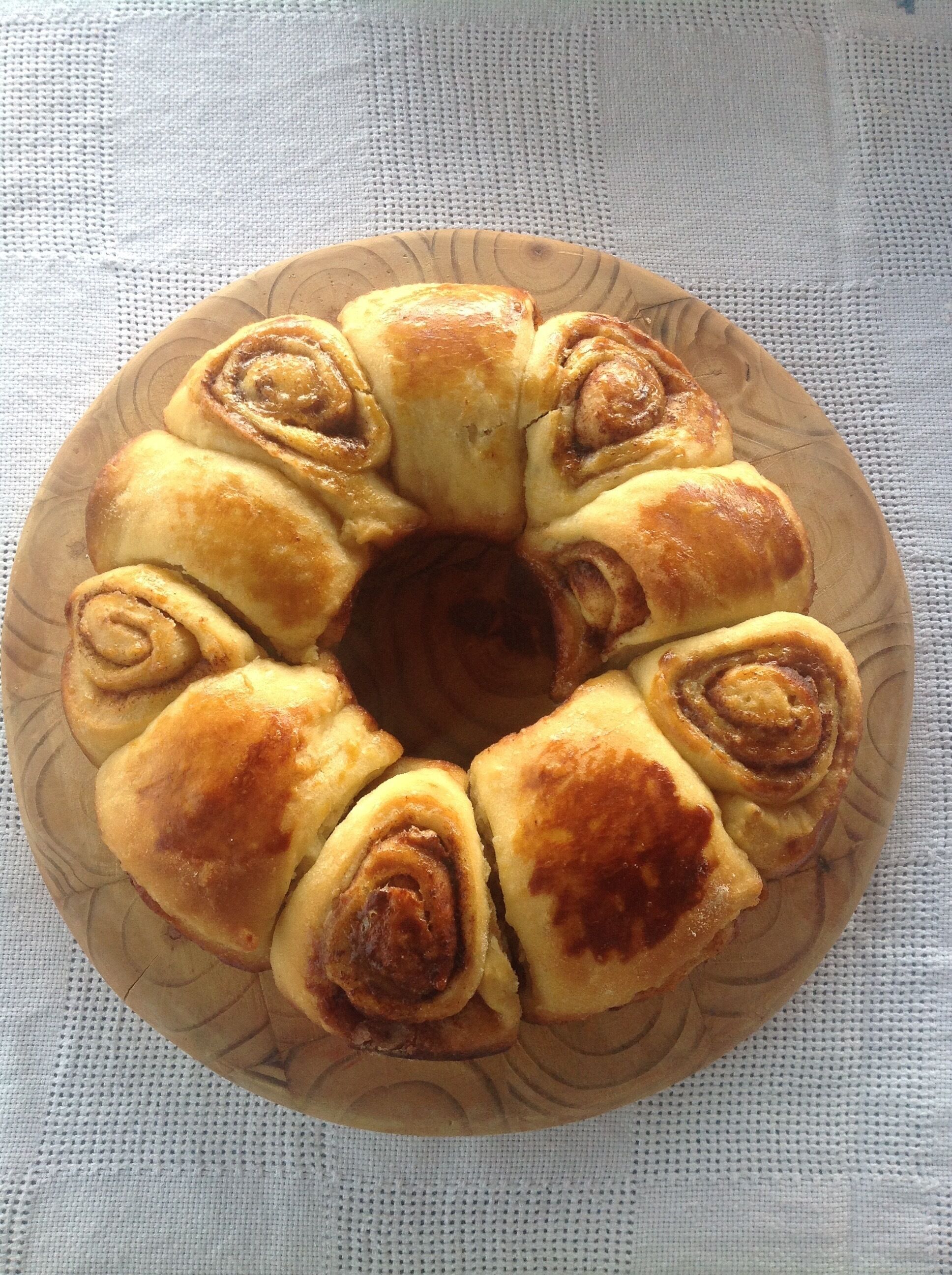 Uma travessa de madeira com um pastelaria de canela sobre um tecido branco texturizado.