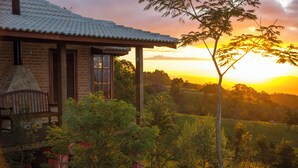 A rustic house with a stone chimney, wooden porch, and a view of a sunset over a grassy landscape. - Magnificat Cottage (Cunha)