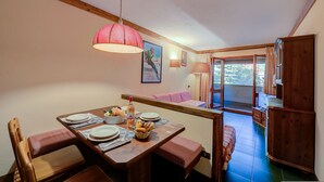 A dining area with a wooden table set for four, a pink lamp, and a view of the outdoors through a window. - Grange Hike Ski - 37C Sestriere (Sauze di Cesana)