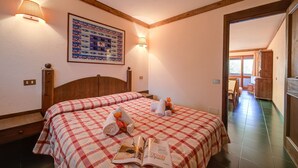 A hotel room with two beds, a wooden headboard, a wall-mounted lamp, a framed picture, and a magazine on the bed. - Grange Hike Ski - 37C Sestriere (Sauze di Cesana)