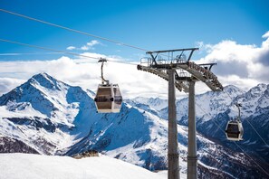 Eine Seilbahn in einer Berglandschaft mit schneebedeckten Gipfeln und blauem Himmel.