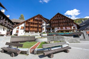 Ein traditionelles Holzhaus mit Balkonen, Steinstufen und einer gepflasterten Fläche mit Bänken.