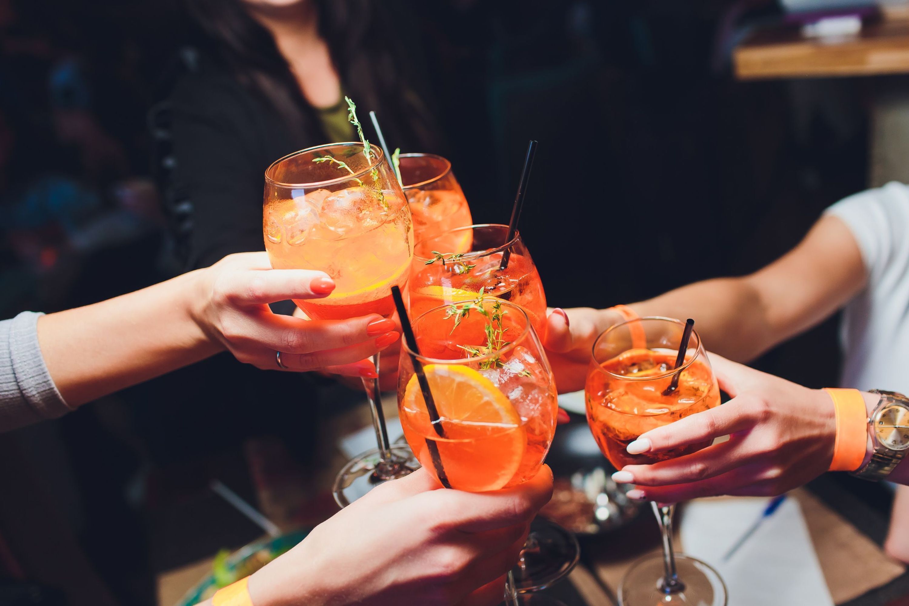 Un groupe de personnes tenant des verres contenant une boisson, décorés d’une tranche d’orange et d’une branche d’herbe aromatique.