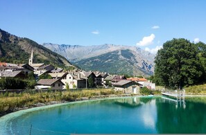 A lakeside village with traditional buildings, a church, and mountains in the background. - Le Meubl Between City Center Skiing (Bardonecchia)