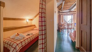 Een slaapkamer met een bed, nachtkastje en een raam met gordijnen. Er is een houten deur en een trap die naar een andere kamer leidt.