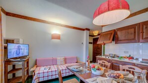 A cozy living room with a sofa, wooden dining table set for a meal, and a kitchen area with cabinets and a stove.