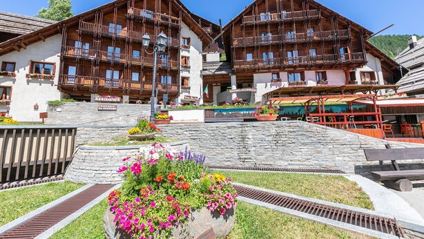 A traditional wooden chalet with balconies, a stone pathway, and flower beds.