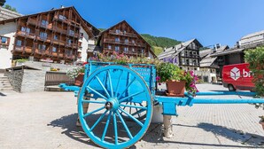 A traditional wooden building with balconies, a blue carriage, and a red van parked nearby.