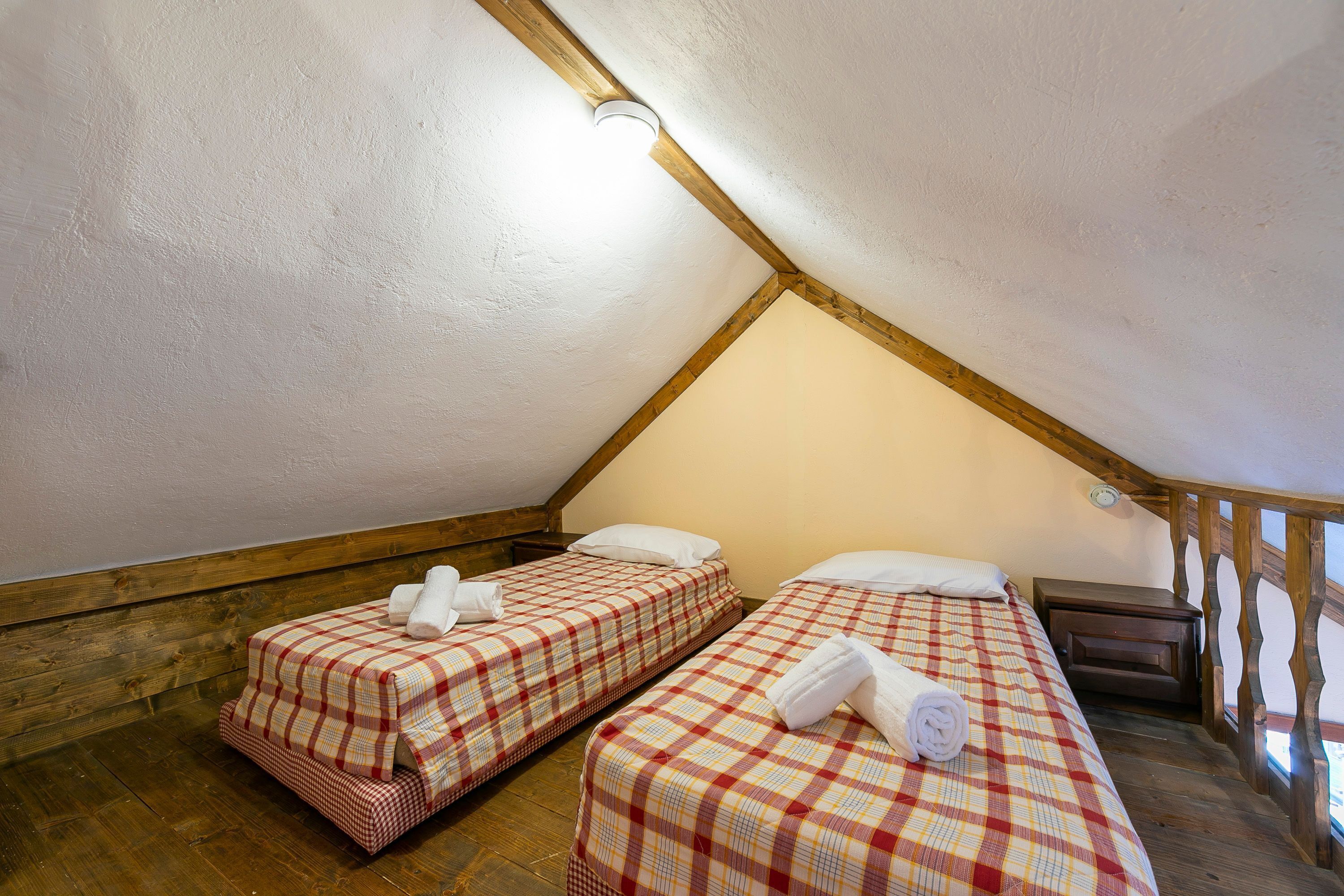 A small, cozy attic bedroom with two beds, wooden beams, and a sloped ceiling.