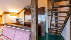 Een gezellige kamer met een bed, een houten trap en een keukenhoek met kastjes en een magnetron.