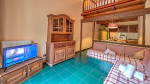 A cozy living room with a wooden cabinet, a television, a checkered sofa, and a balcony with a wooden railing.