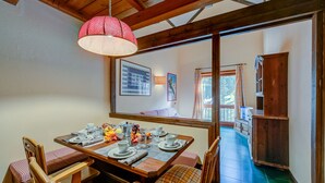 A dining area with a wooden table set for four, a red polka-dotted lamp, and a view of a balcony through a window.