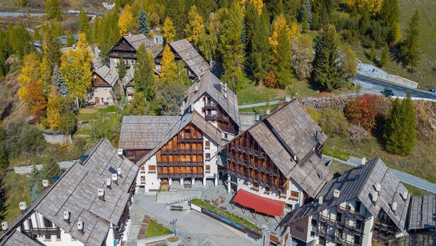 A traditional chalet-style building with multiple balconies, a central courtyard, and a surrounding forested area.