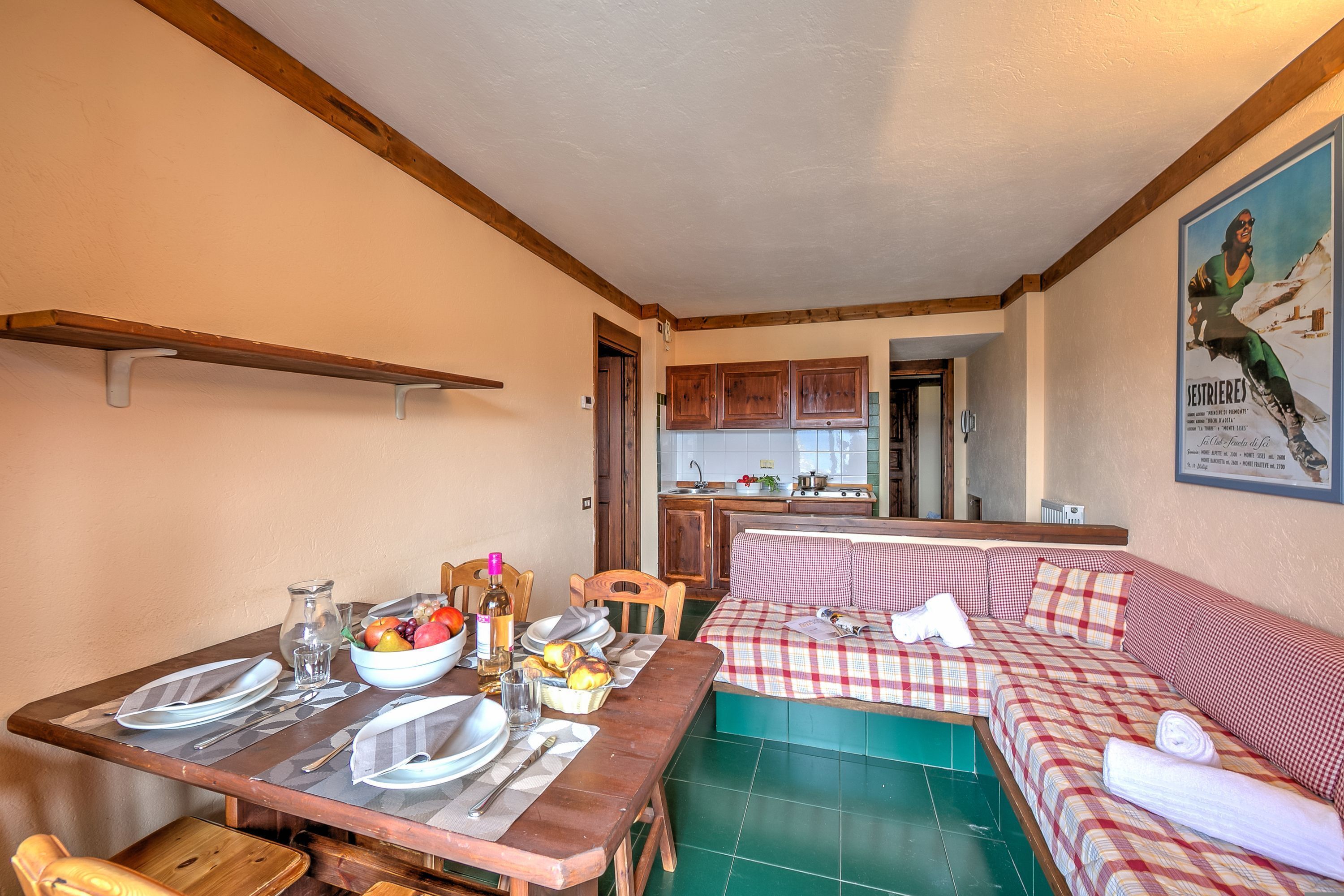 A cozy kitchen with wooden cabinets, a dining table set with plates and cutlery, and a checkered sofa in the living area.