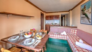 A cozy kitchen with wooden cabinets, a dining table set with plates and cutlery, and a checkered sofa in the living area. - Grange Hike Ski - 26D Sestriere (Sauze di Cesana)