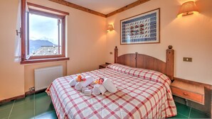 A bedroom with a large bed, a window with curtains, a wall-mounted lamp, and a framed picture. - Grange Hike Ski - 26D Sestriere (Sauze di Cesana)