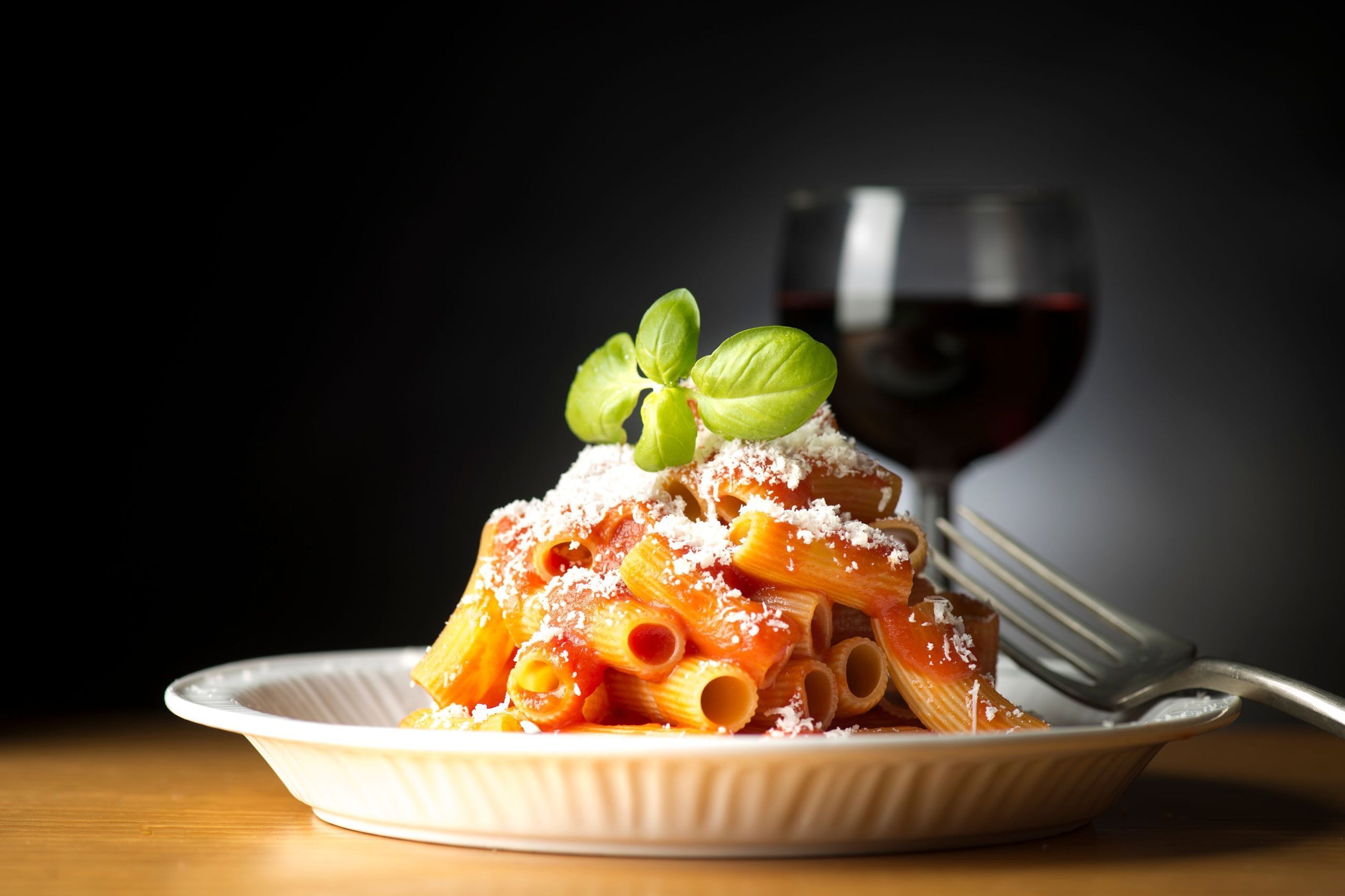 A plate of pasta with a glass of red wine.