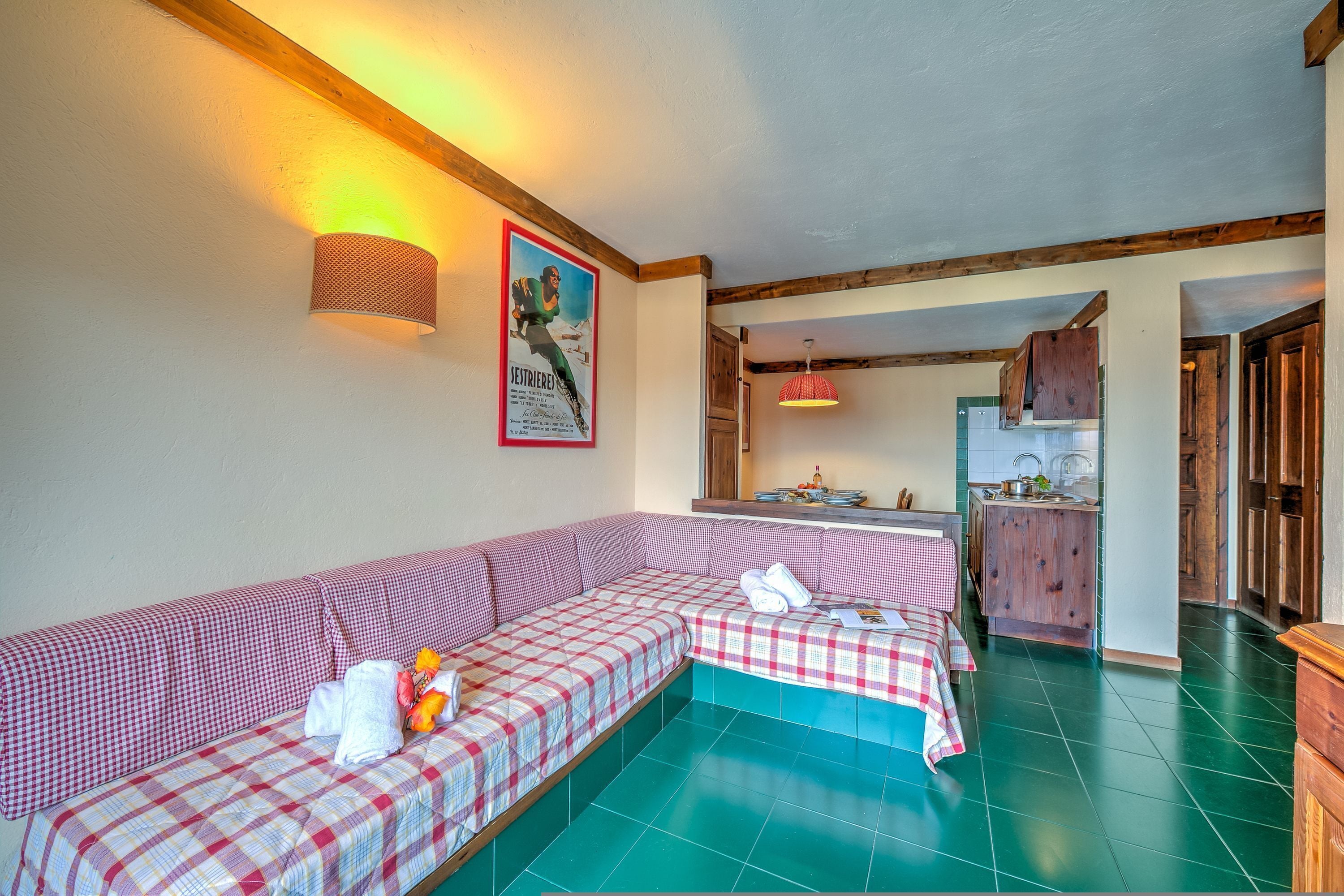 A cozy room with a checkered sofa, a wooden ceiling, and a kitchen area in the background.