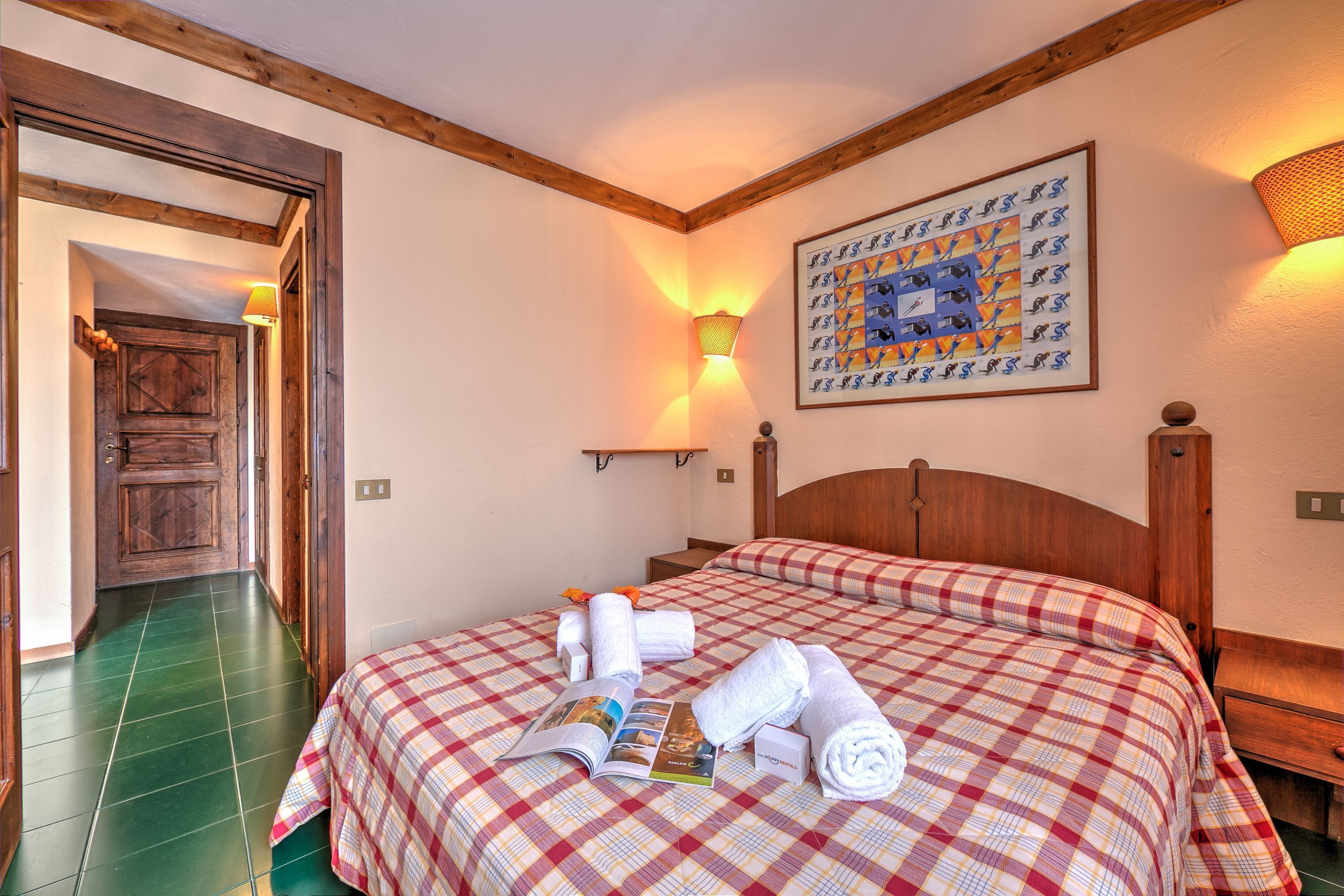 A hotel room with a checkered bedspread, neatly folded towels, and a framed picture on the wall.