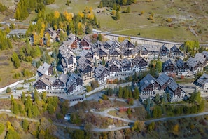 Vue aérienne d’un complexe hôtelier comprenant plusieurs bâtiments de style chalet, entourés d’arbres et bordés d’une petite route.