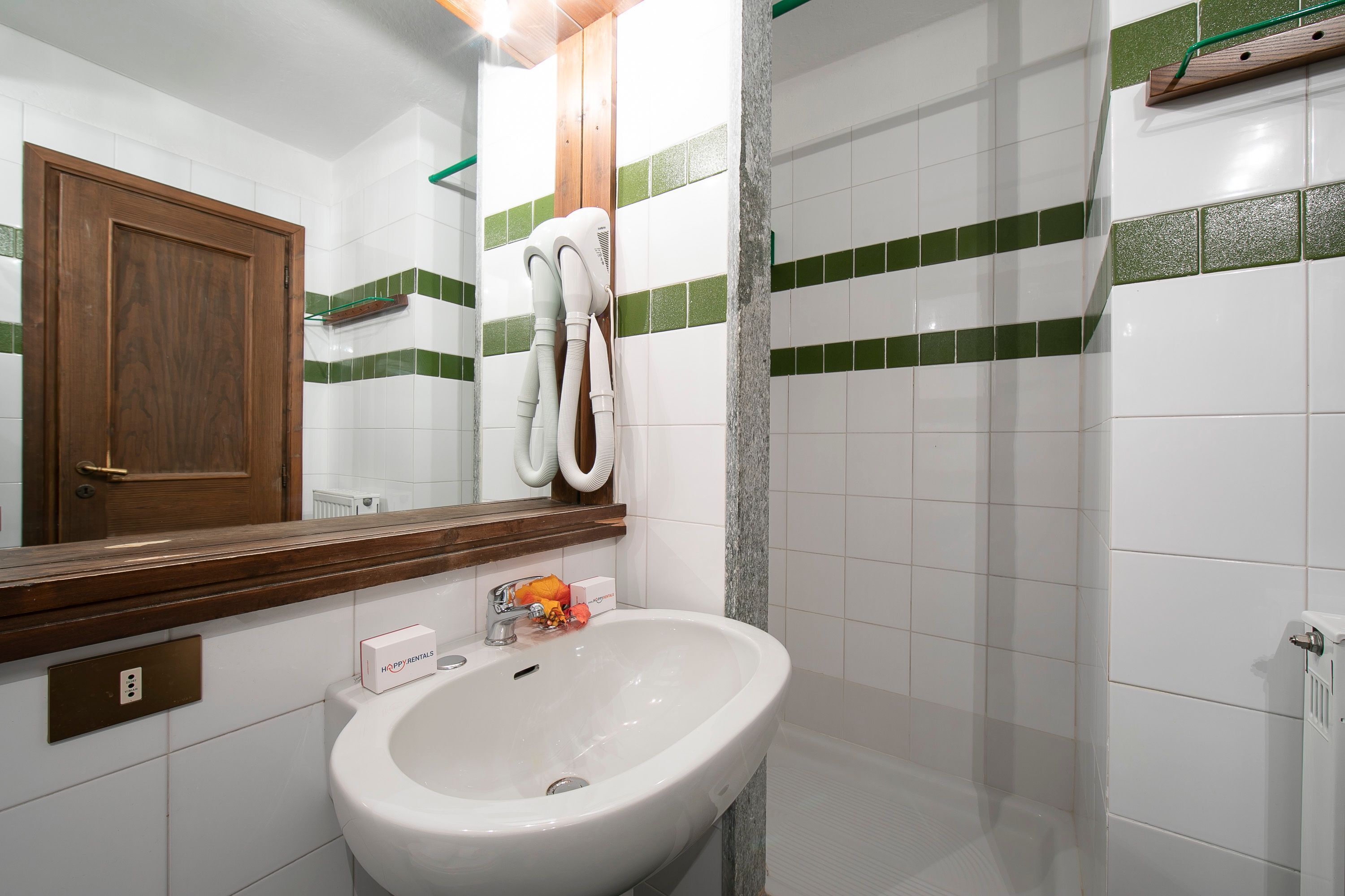 A bathroom with a white sink, a wooden door, and green-tiled walls.
