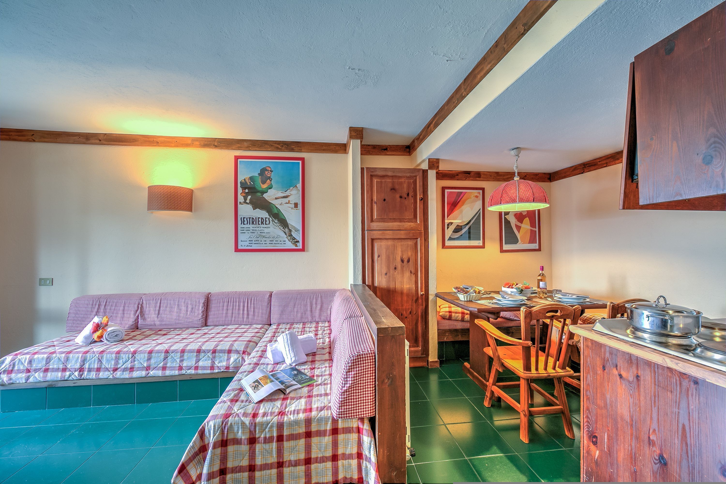 A cozy room with a checkered bed, wooden furniture, and a dining area with a table and chairs.