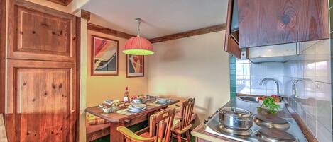 A kitchen with wooden cabinets, a dining table with chairs, a hanging light fixture, and a sink.