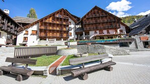 Un edificio tradizionale in legno con balconi, un vialetto in pietra e una panchina di legno in un ambiente esterno soleggiato.