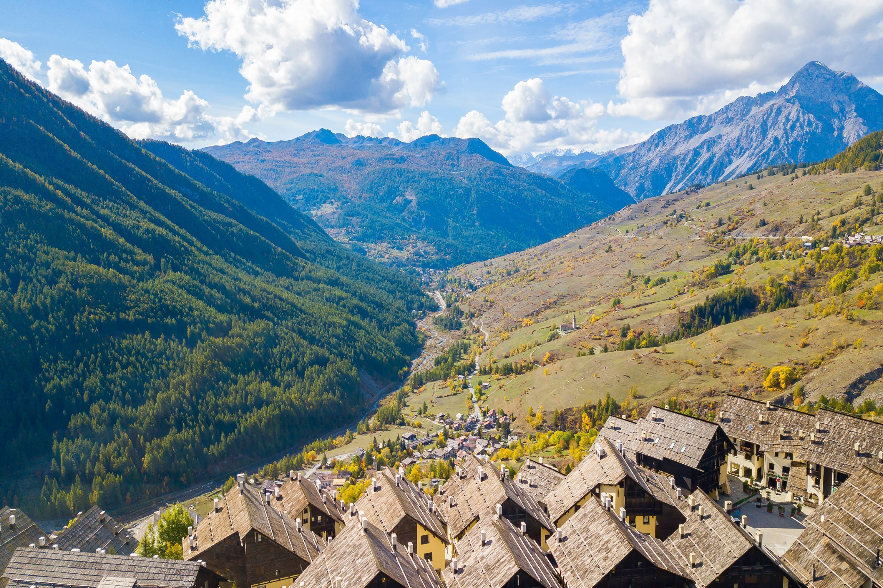 A mountainous village with traditional wooden houses, a valley, and distant mountains.