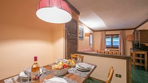 Zona pranzo con tavolo di legno apparecchiato per due, una bottiglia di vino e una ciotola di frutta.