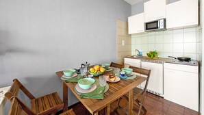A dining area with a wooden table set for four, surrounded by chairs. A microwave and a small kitchen area with a sink and stove are visible in the background. - La Porta Sul Mare Sea View (Ospedaletti)