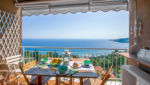 A balcony with a table set for a meal, overlooking a scenic view of the sea. - La Porta Sul Mare Sea View (Ospedaletti)