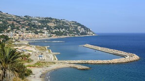 A coastal town with a beach, a rocky breakwater, and buildings on a hillside. - La Porta Sul Mare Sea View (Ospedaletti)