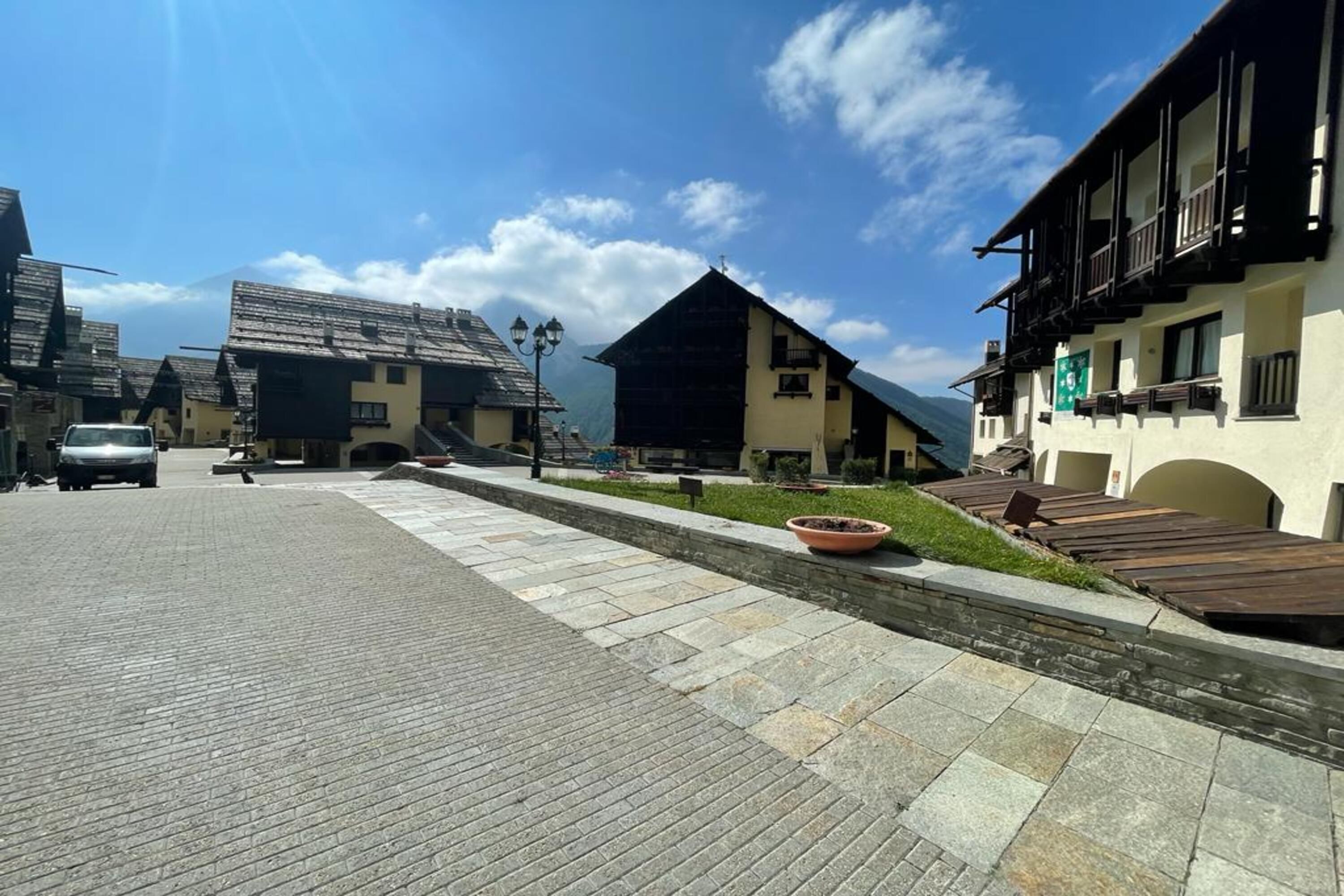 A traditional mountain village with stone-paved streets, wooden buildings, and a clear blue sky.