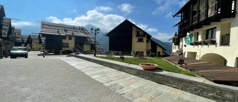 A traditional mountain village with stone-paved streets, wooden buildings, and a clear blue sky.