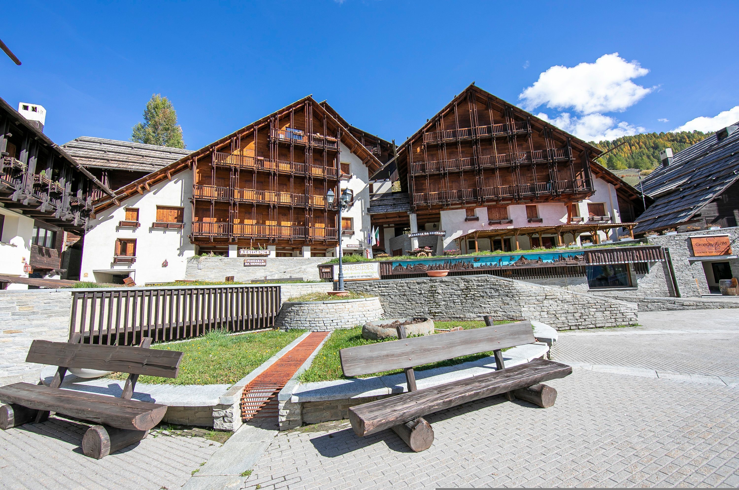A traditional wooden building with balconies, a stone pathway, and wooden benches.