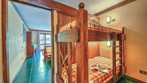 A bunk bed with a plaid bedspread, wooden headboard, and a small table with a book. - Grange Hike Ski - 30D Sestriere (Sauze di Cesana)